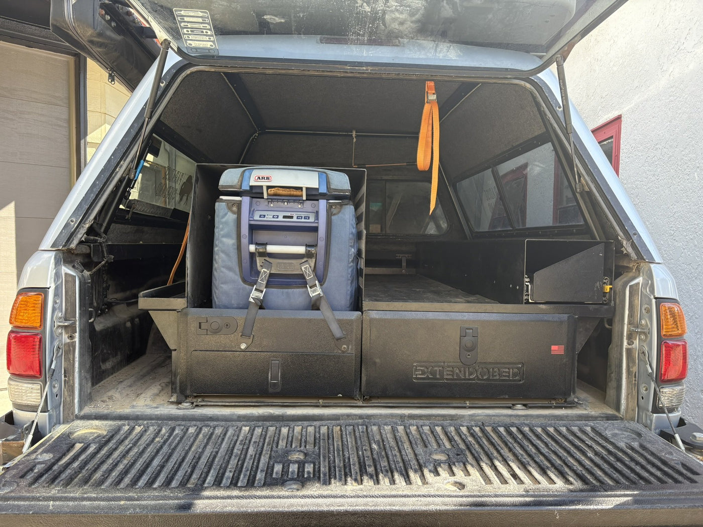 Straight-on view from the open tailgate showing the closed Extendobed drawer fronts with the Extendobed badge and the ARB fridge strapped on its slide — photo 3