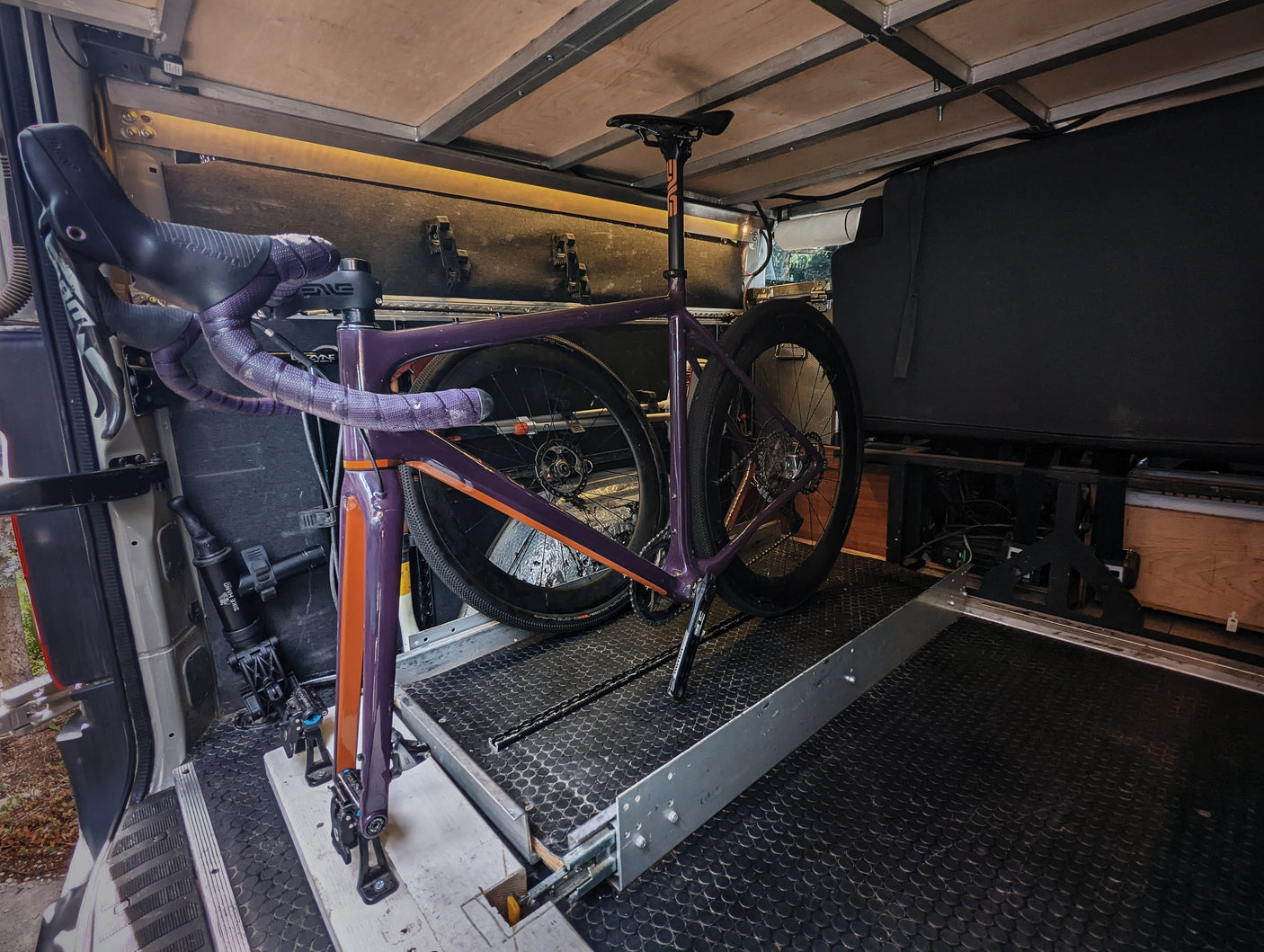 Inside an RV rental, a purple gravel bike is securely mounted on a slide-out tray, optimizing space for travel.