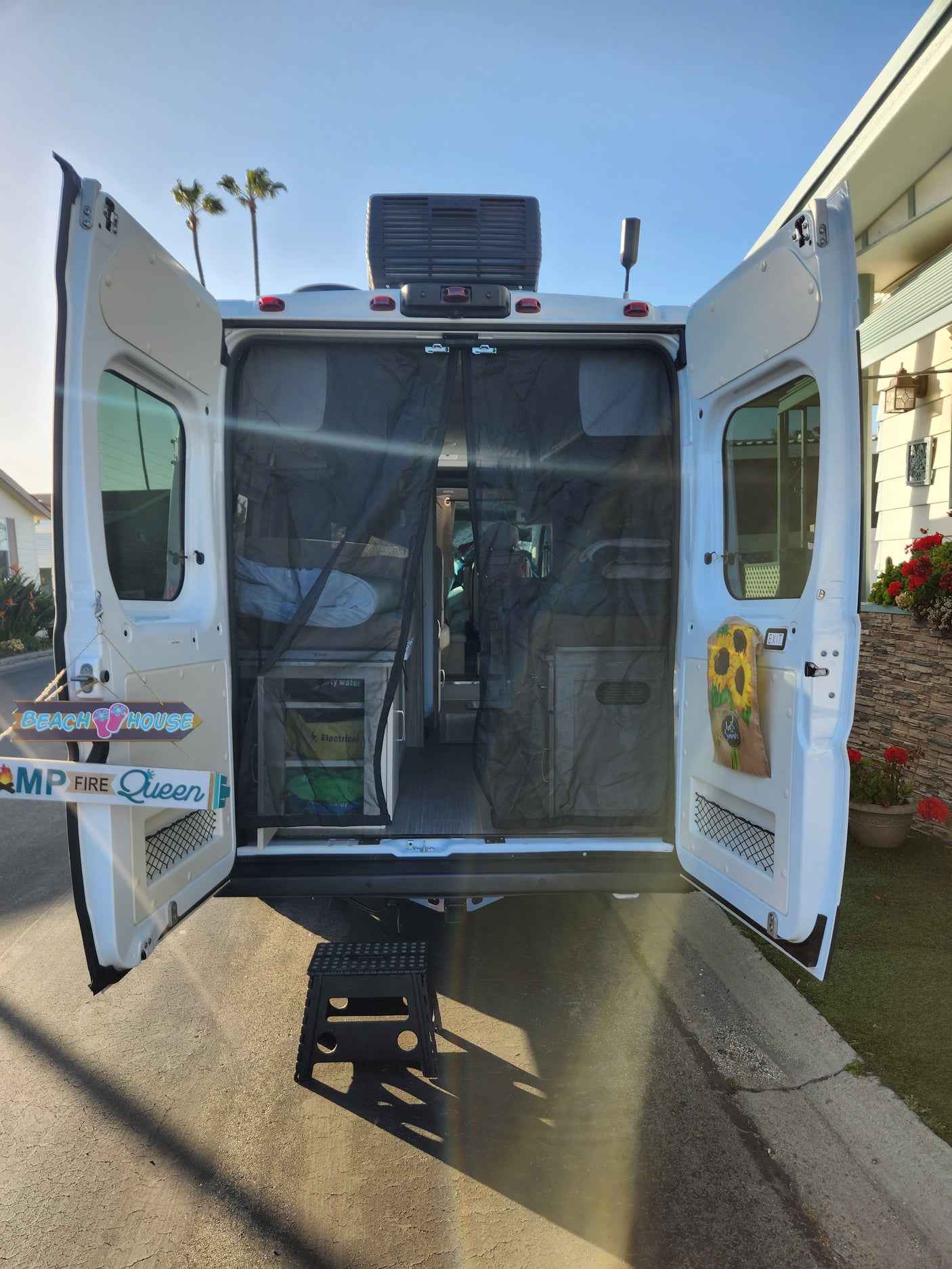 Ready for adventure! White RV rental camper van with open back doors, revealing custom storage and personalized decor.