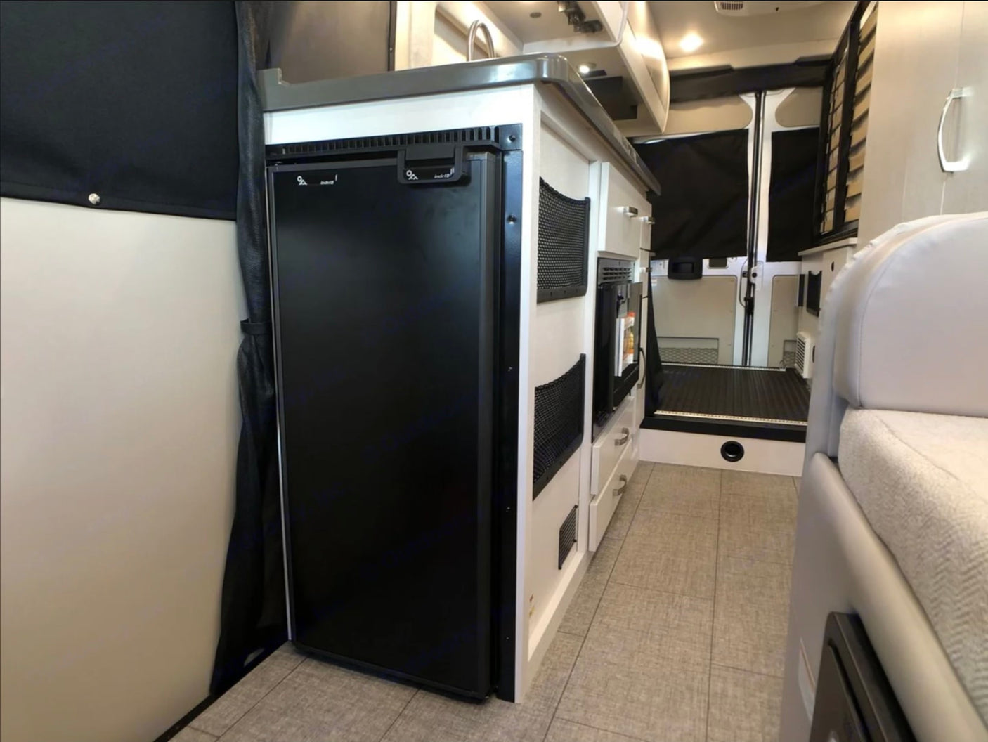 Compact RV rental interior featuring a built-in fridge, kitchenette, and hallway leading to the rear. Ideal for mobile living.