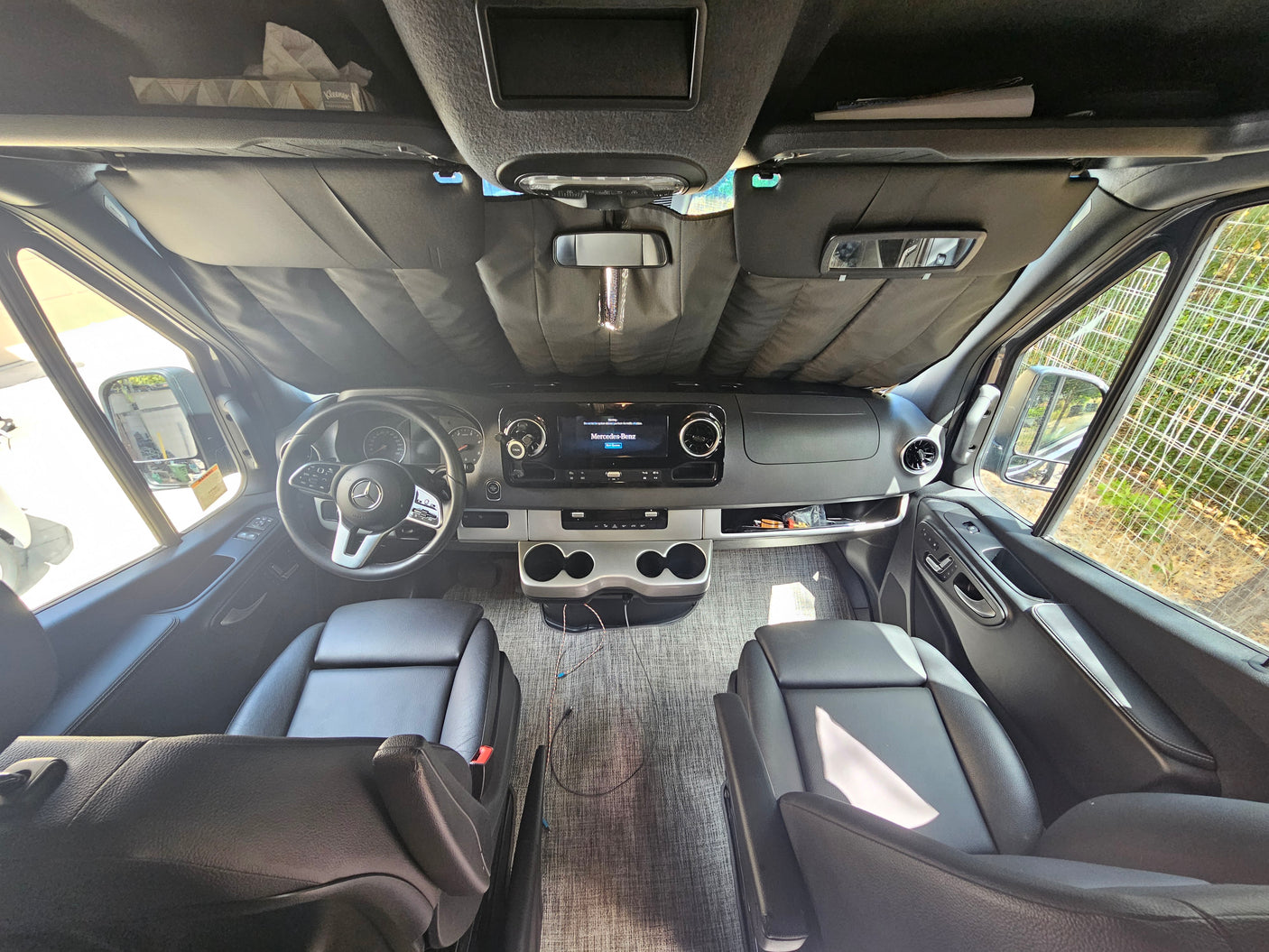 Spacious Mercedes-Benz RV rental cockpit with driver/passenger seats, dashboard, and sunshade.