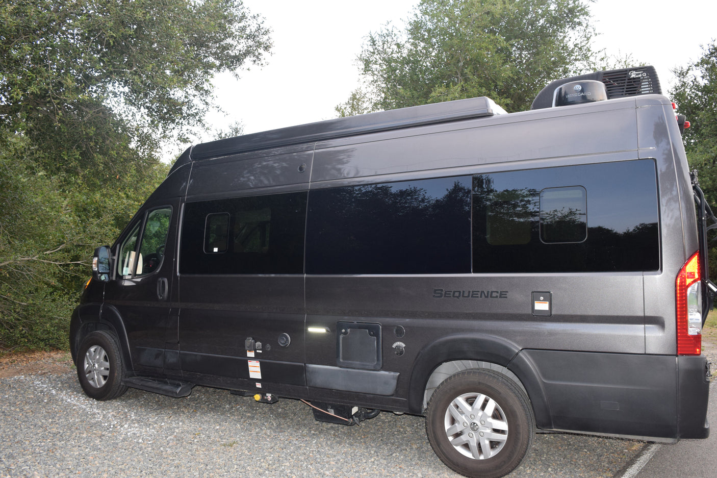 A gray Thor Sequence RV rental (campervan) is parked on gravel beside trees, ready for your next adventure.
