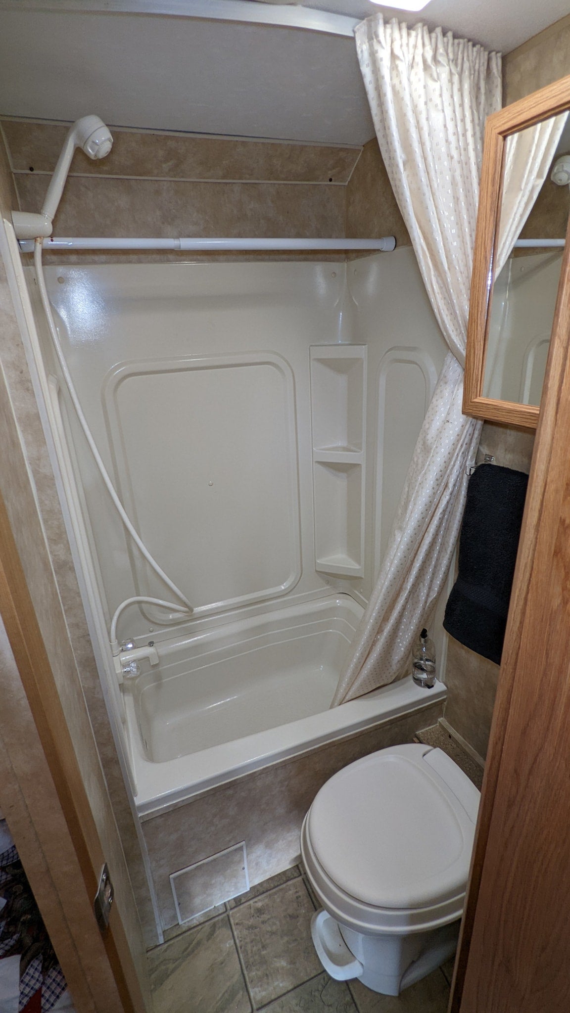 This RV rental's compact bathroom features a bright shower/tub combo, toilet, and mirror, designed for efficiency.