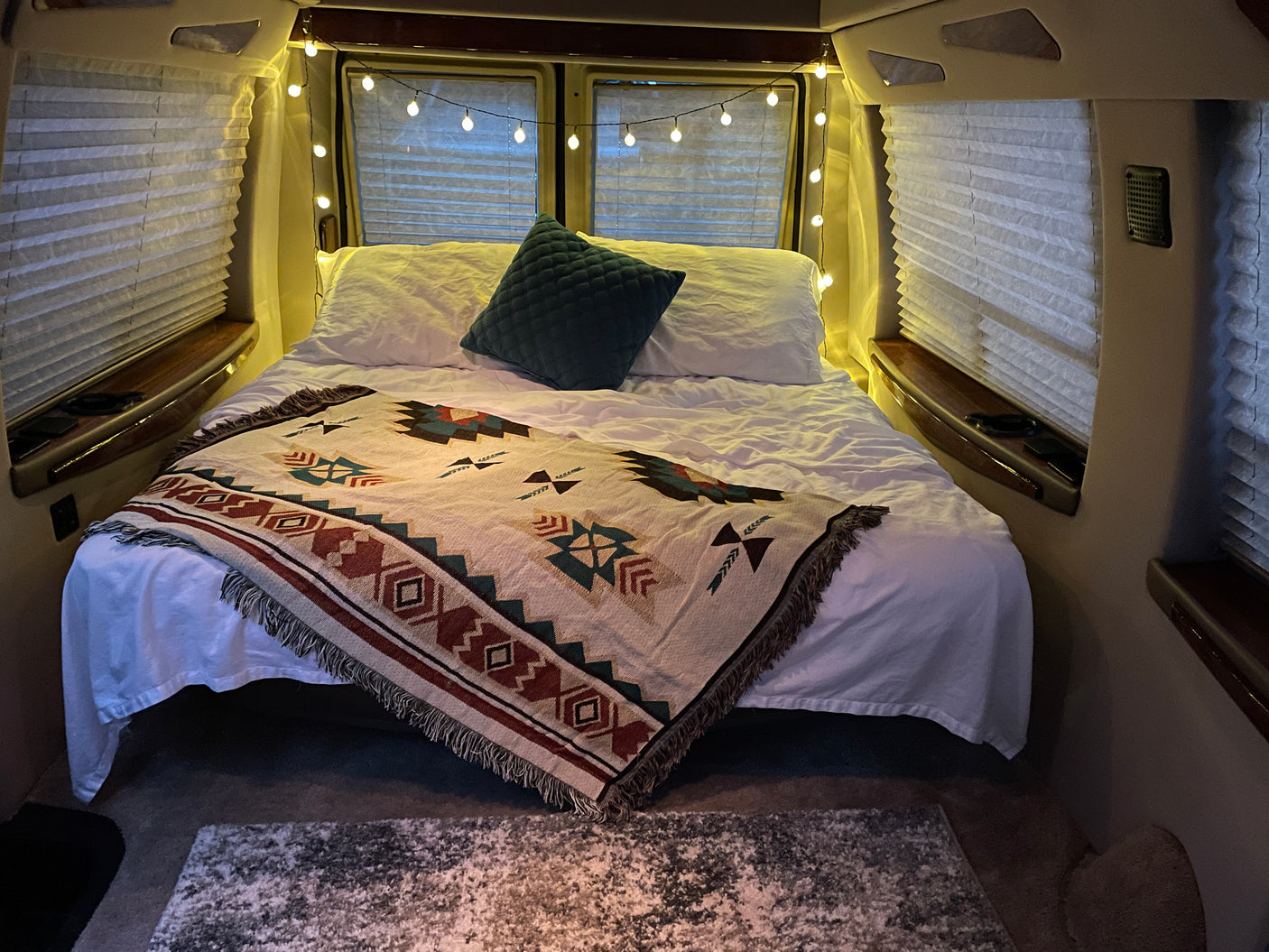 Inviting RV rental bedroom with a comfy bed, Southwestern blanket, ambient string lights, and pleated window blinds.