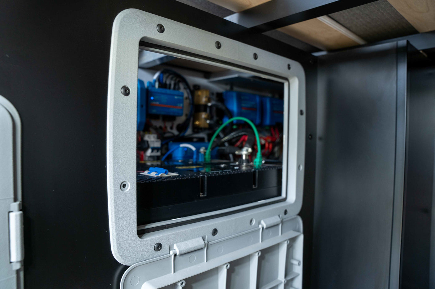 An open access panel inside an RV rental reveals the essential electrical power system with blue components and wiring.