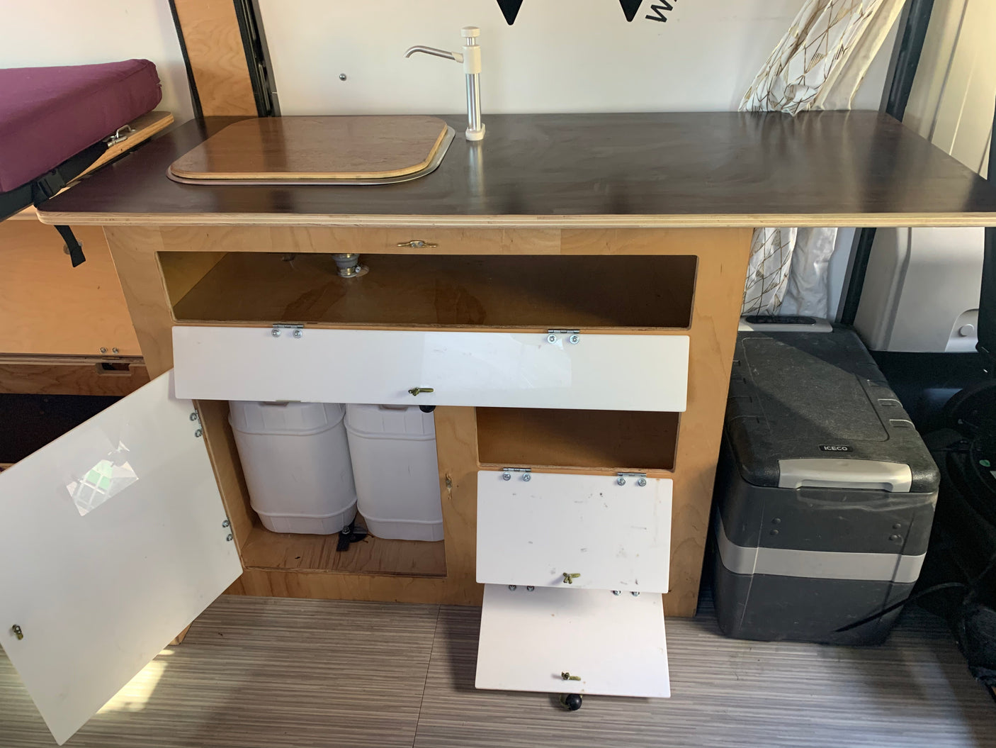 RV rental: A compact van kitchenette with a sink, water tanks, and an ICECO portable fridge for off-grid living.