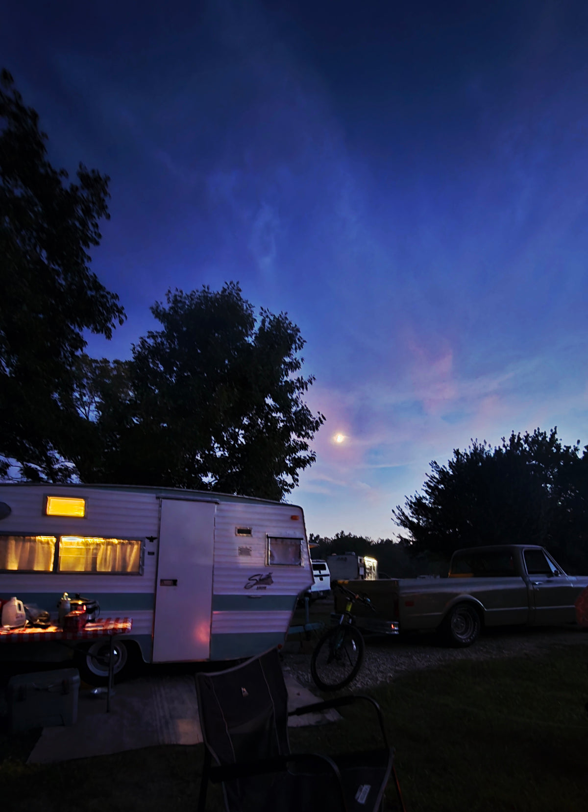 Twilight RV rental camping scene with a vintage trailer, truck, and moon visible in the deep blue and pink sky. — photo 5