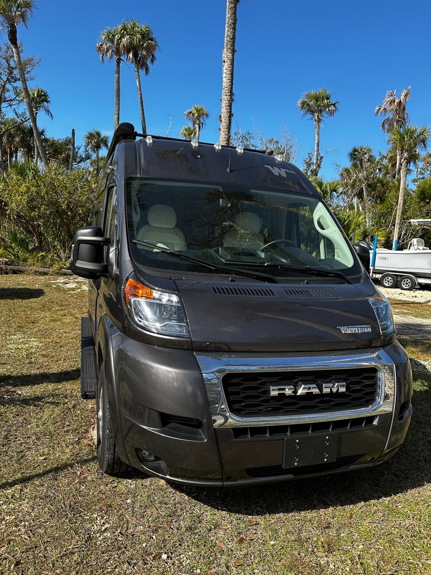 An RV rental: a sleek gray Ram ProMaster camper van parked outdoors under palm trees.