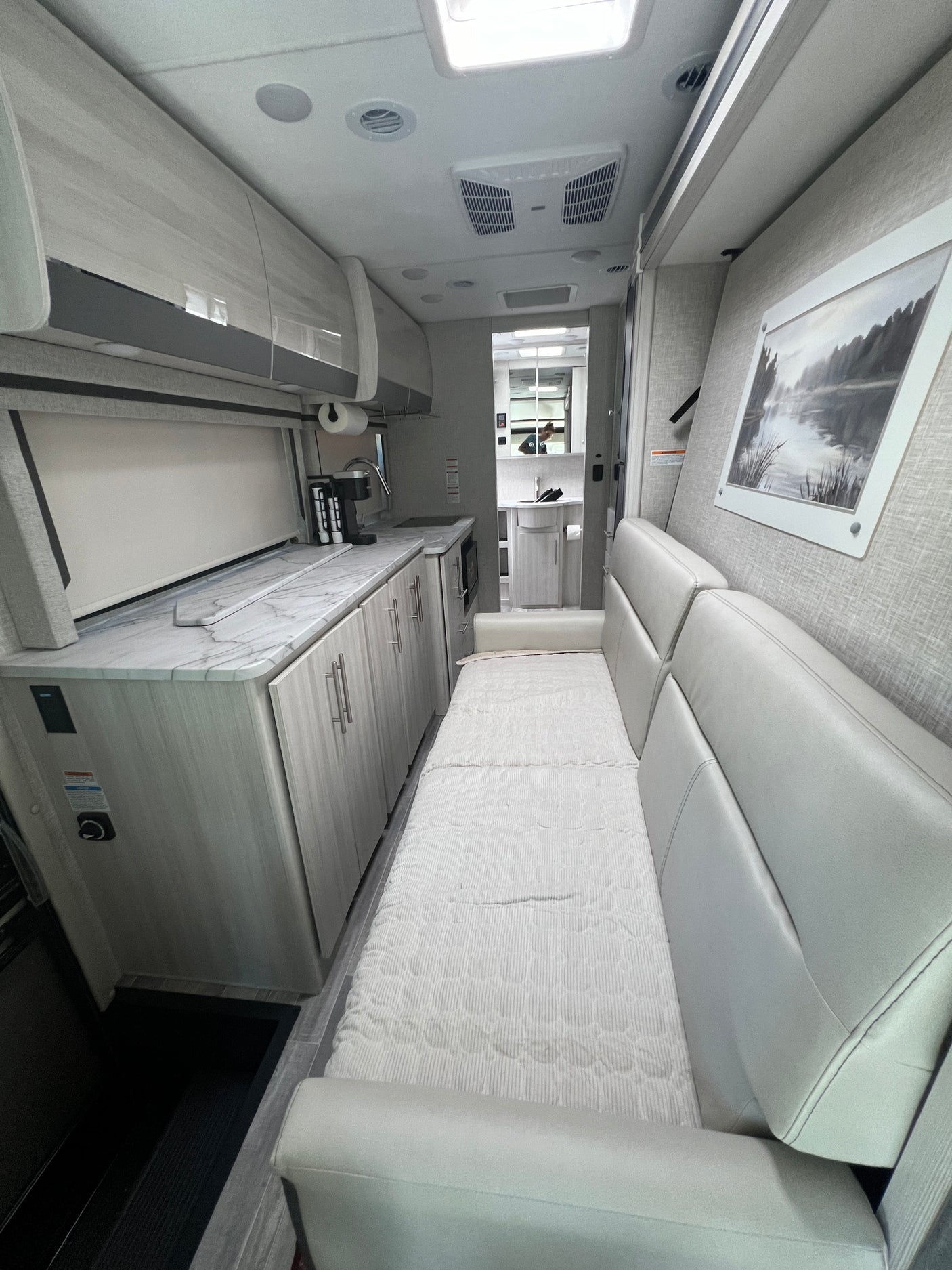 View inside a modern RV rental: long light sofa/bed, light wood cabinets, and kitchen area with marble-look counter.