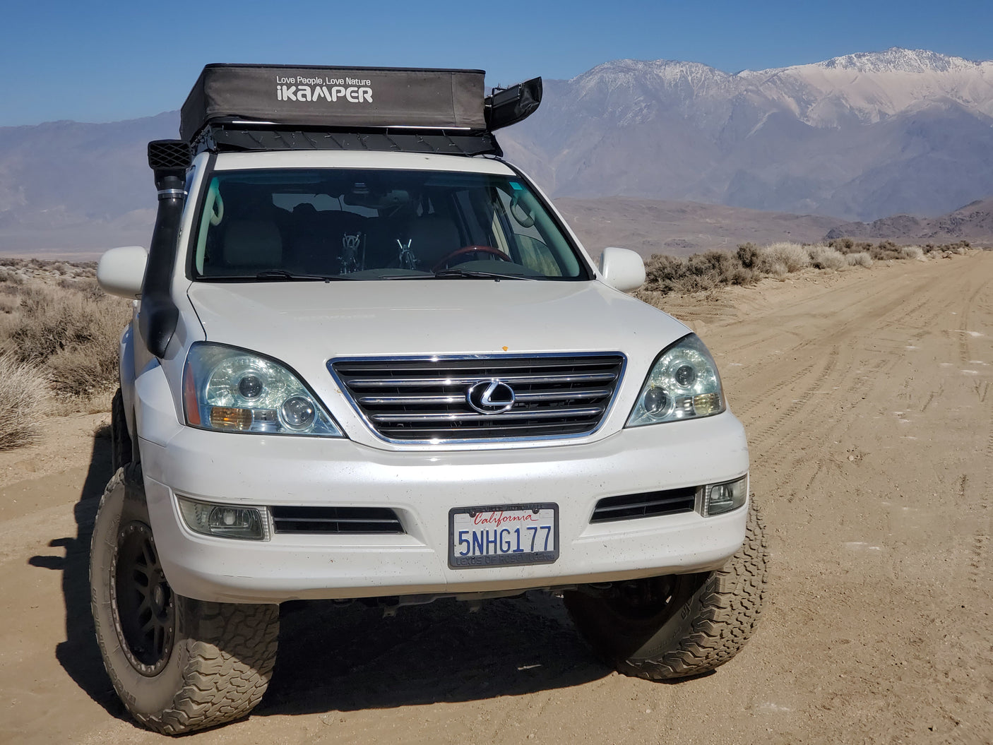 White Lexus SUV modified for overlanding with an iKamper rooftop tent on a dirt trail, a rugged RV rental alternative.