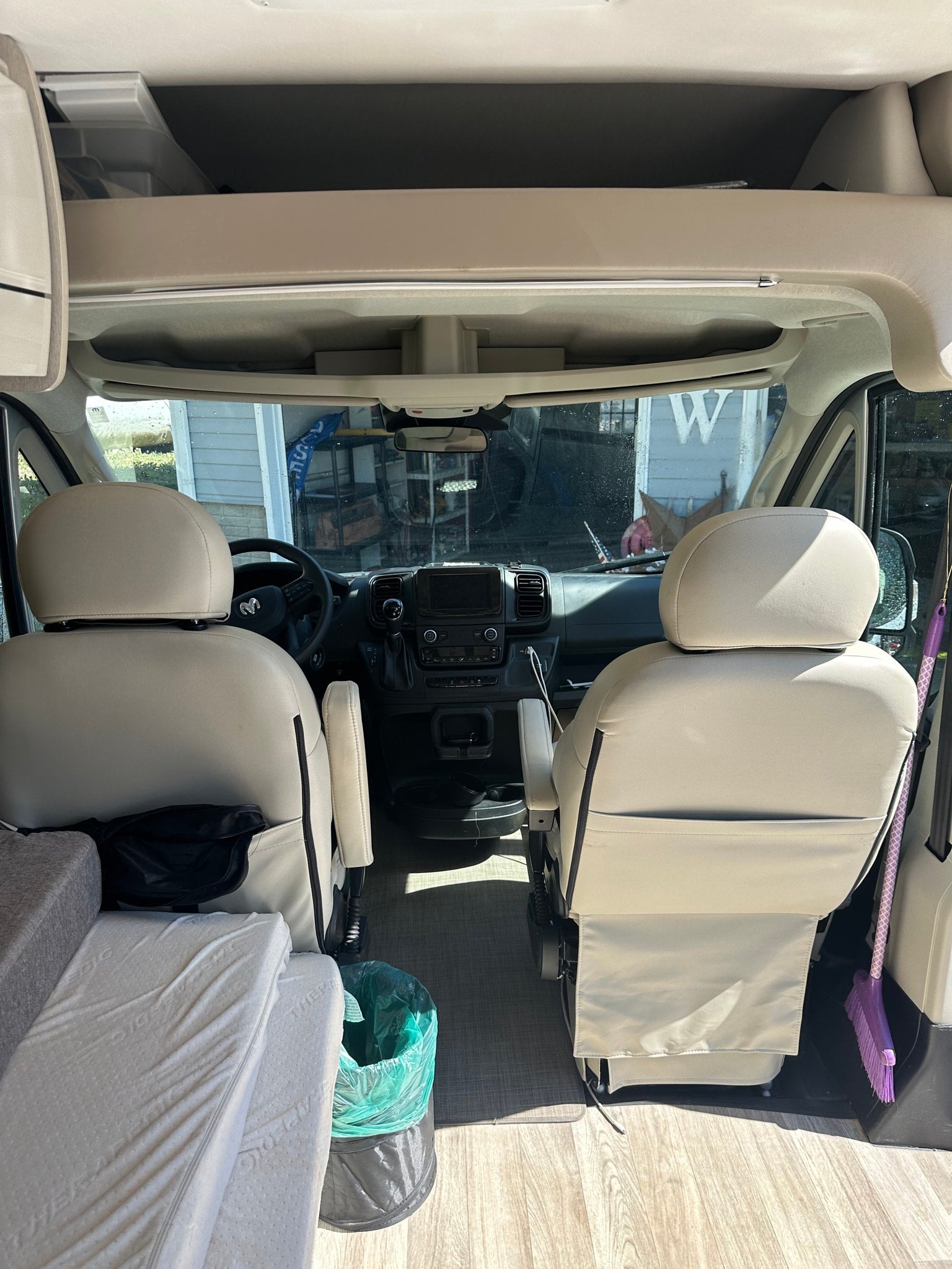 View inside an RV rental looking forward, featuring the cockpit with swivel seats, dashboard, overhead storage, and adjacent living area.