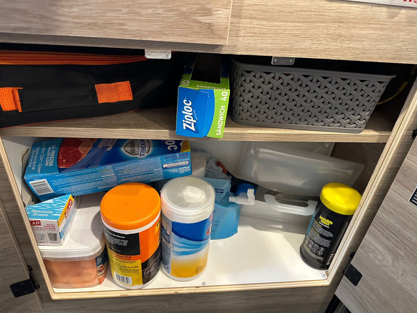 This RV rental cabinet features organized kitchen and cleaning supplies: Ziploc bags, wipes, and storage solutions for travel.