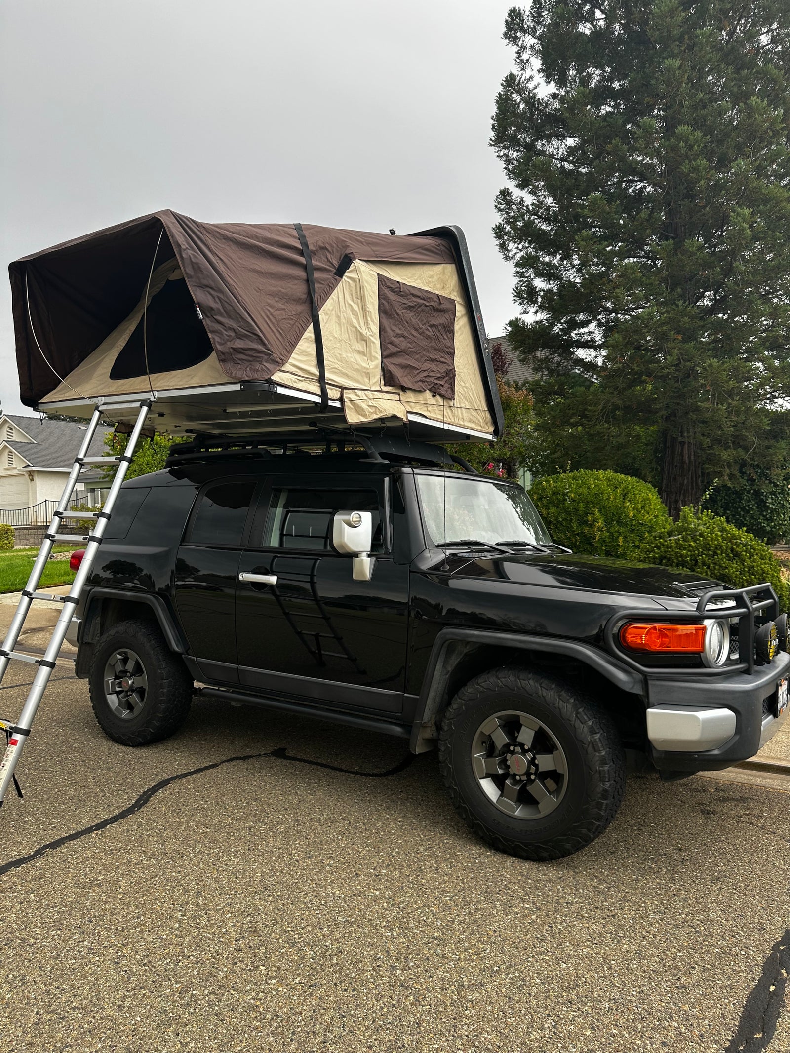 Black FJ Cruiser with a brown rooftop tent deployed, ladder extended. Perfect for an adventure rv rental.