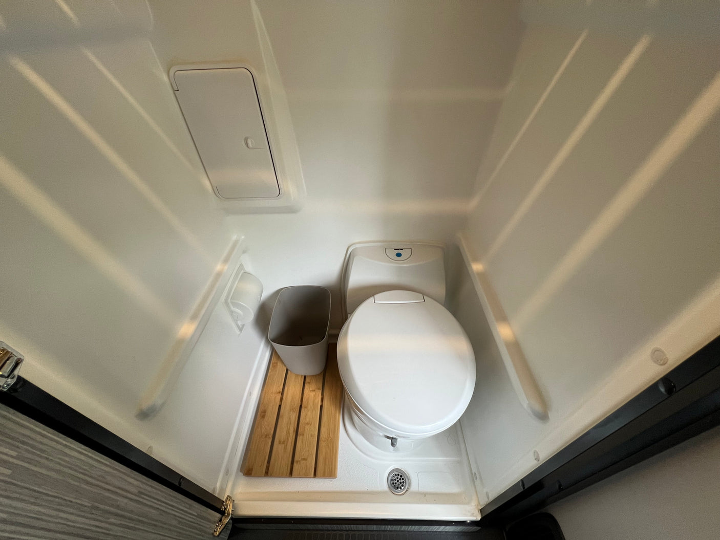 Compact RV rental wet bath with toilet, wooden floor mat, and drain for practical use.