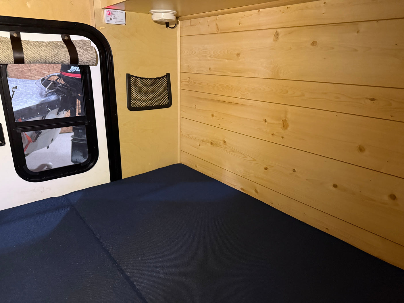 RV rental sleeping area: a dark blue mattress, light wood paneling, and a window with a view of a boat.