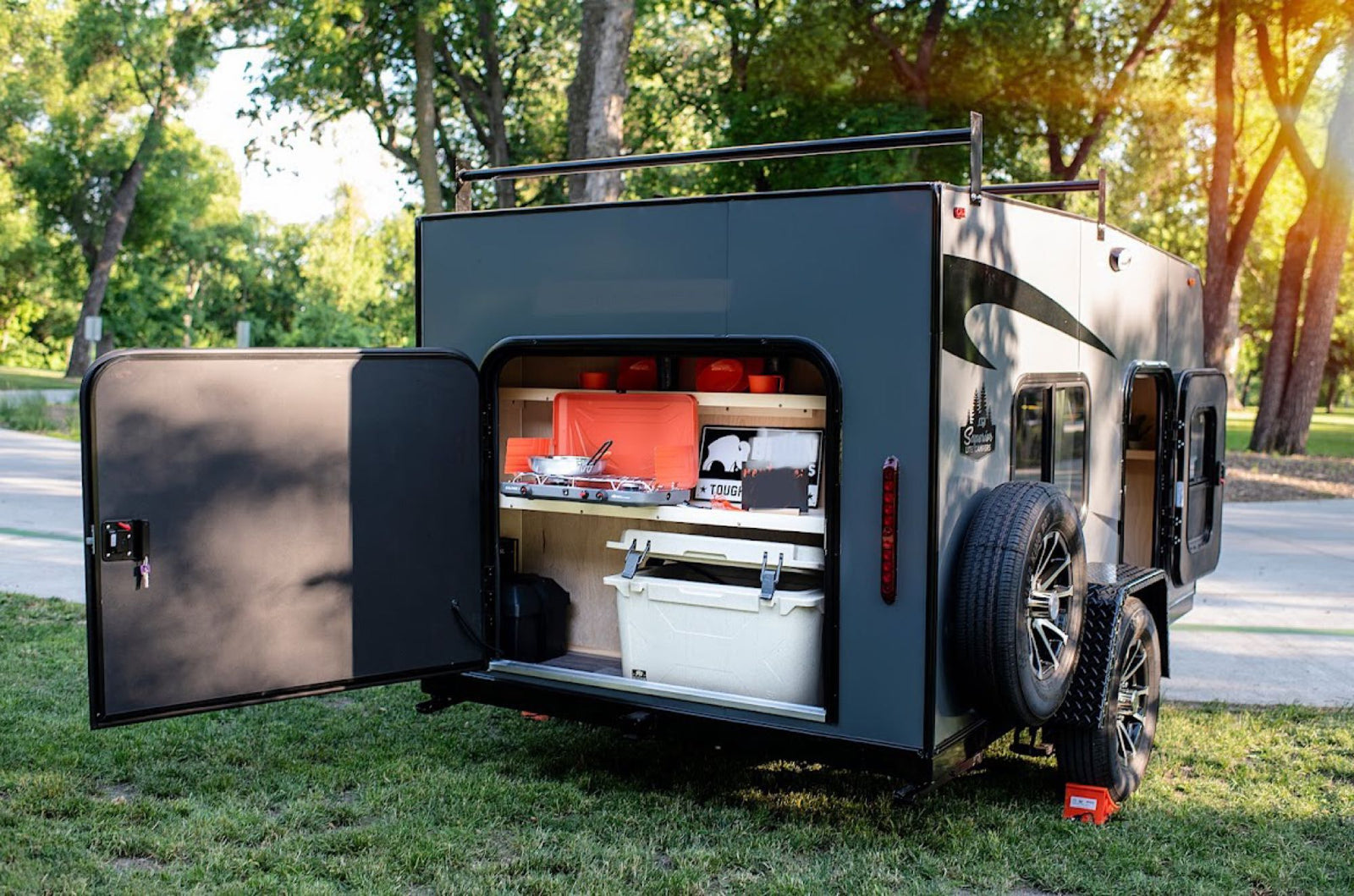 dark grey teardrop-style RV rental sits on a concrete pad at a sunny campsite