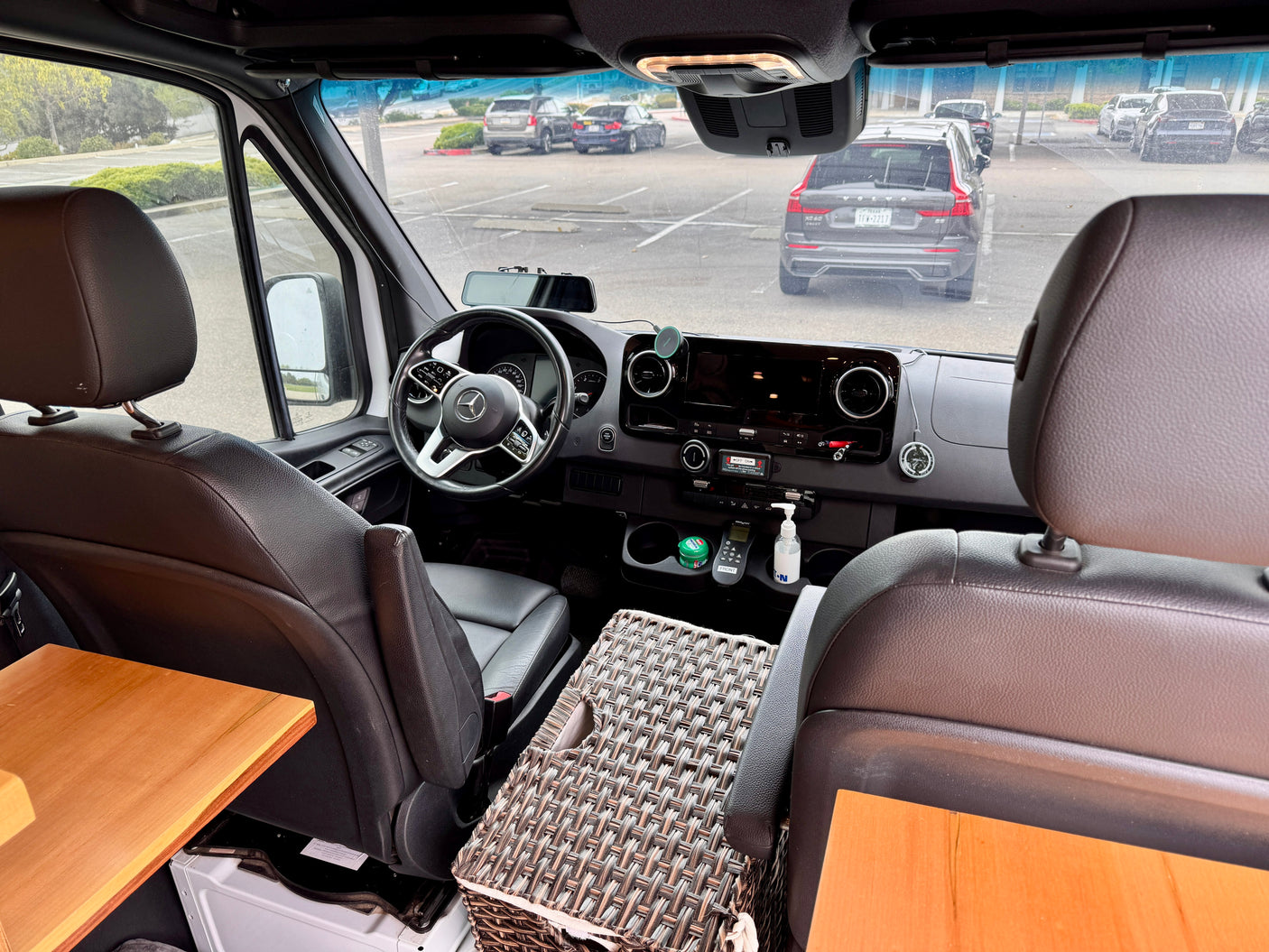 Interior of a well-equipped RV rental showing the Mercedes-Benz driver's area, custom amenities, and parked cars outside.