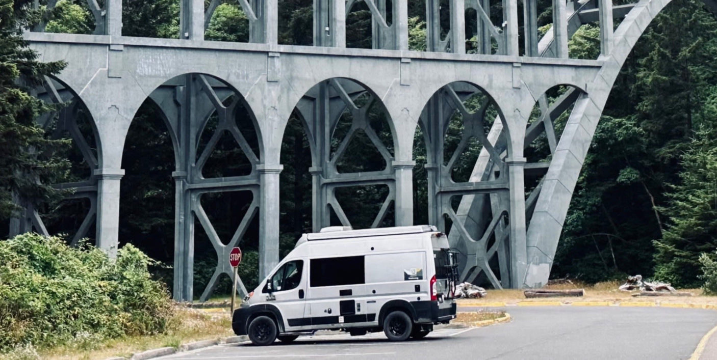An RV rental camper van parked under a historic arched concrete bridge