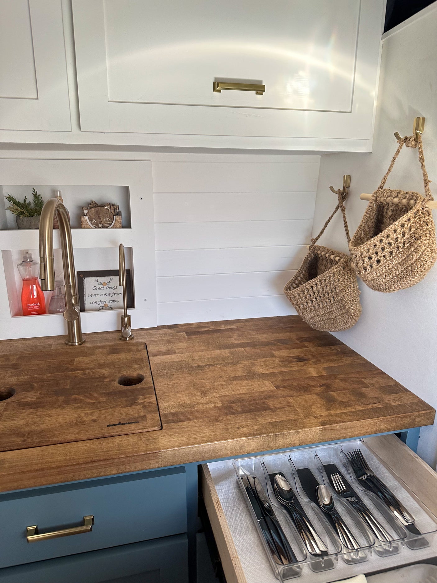 Compact RV rental kitchen featuring a wood countertop, brass faucet, and an open, organized cutlery drawer.
