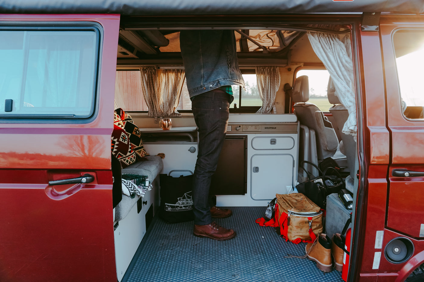 Inside an RV rental: a person stands in a Westfalia camper van, showing the functional kitchen, built-in seating, and travel gear.