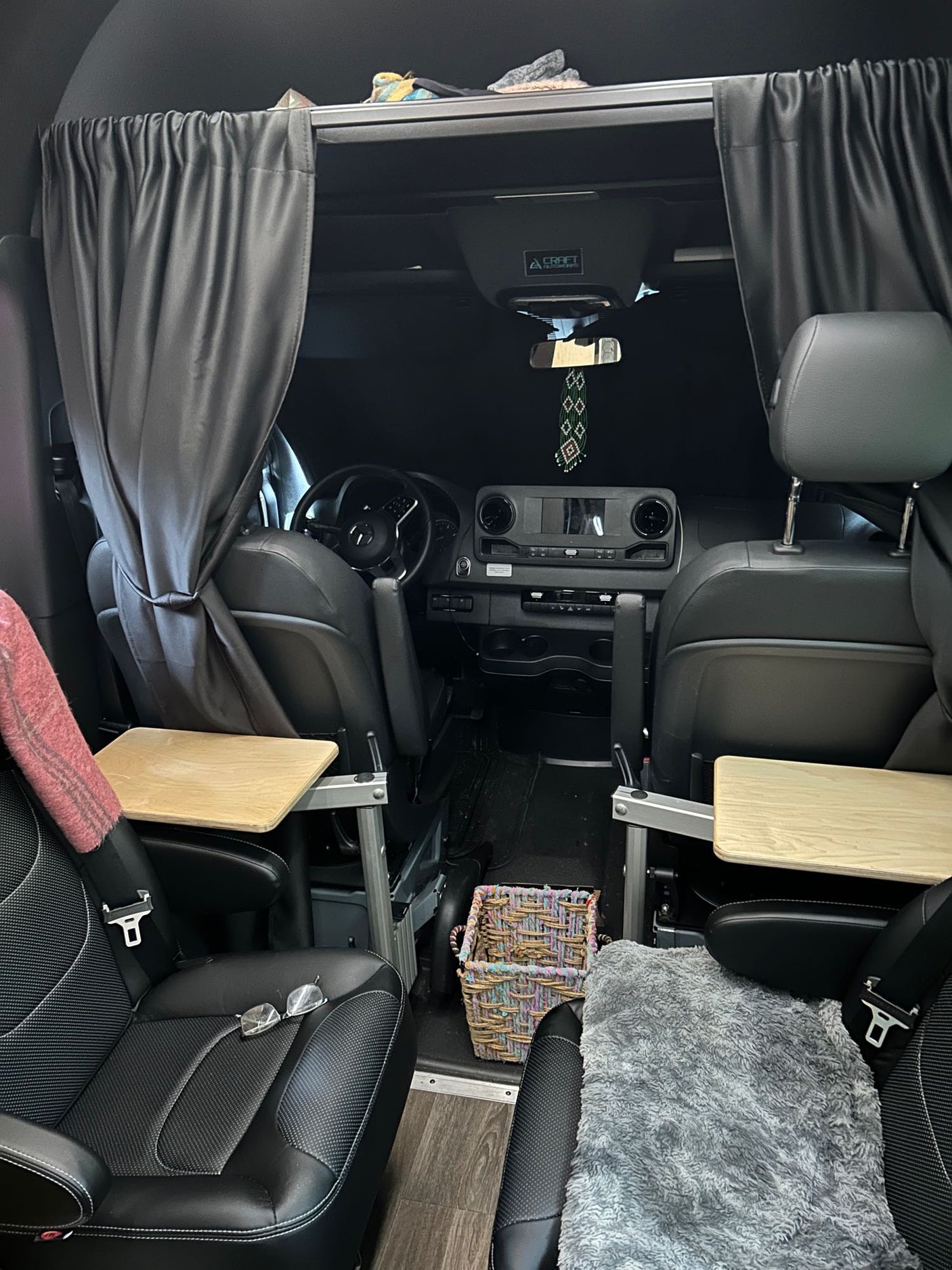 View of an rv rental interior from the rear, showing swiveling front seats with attached tables and privacy curtains.