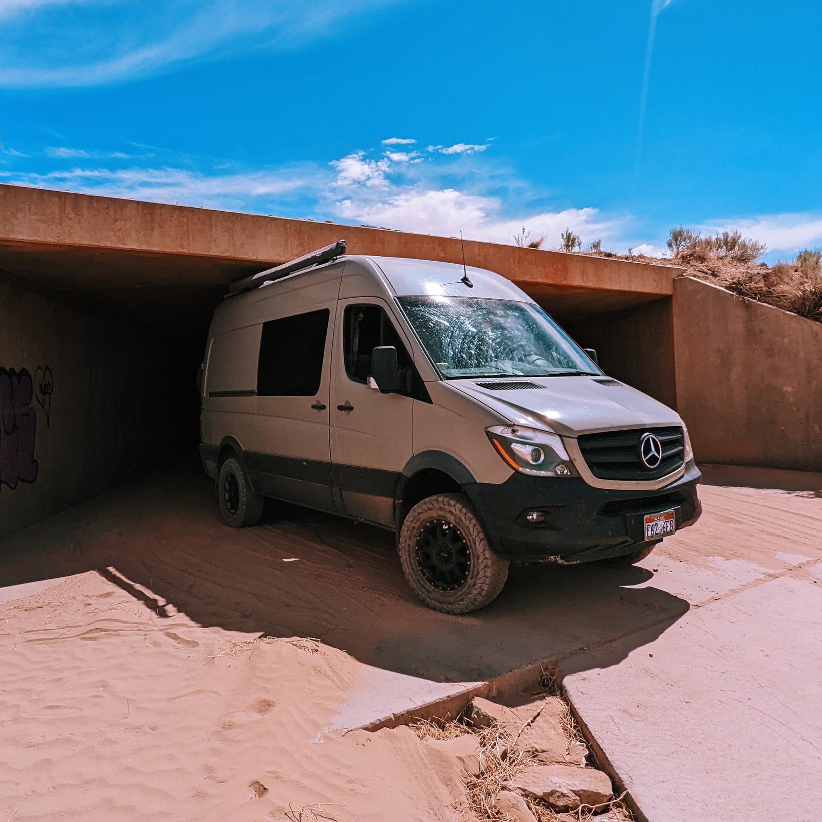 A rugged, off-road rv rental Mercedes Sprinter van navigates a sandy underpass. Perfect for desert adventures!