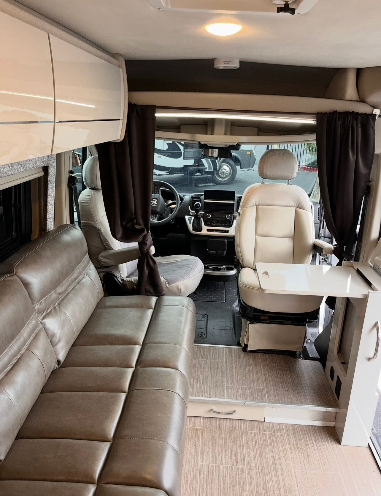Modern RV rental interior: view of the living area with a taupe sofa, cream cab seats, and a swivel table.