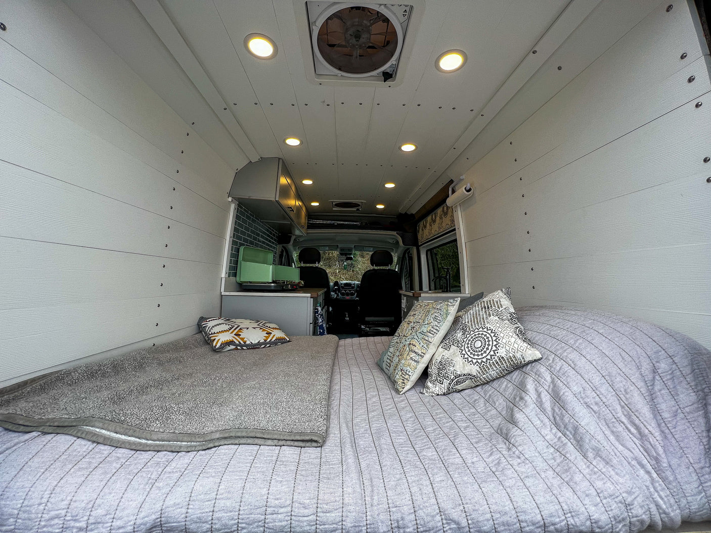 Cozy RV rental interior with a bed, kitchenette, and wood paneling, seen from the back.