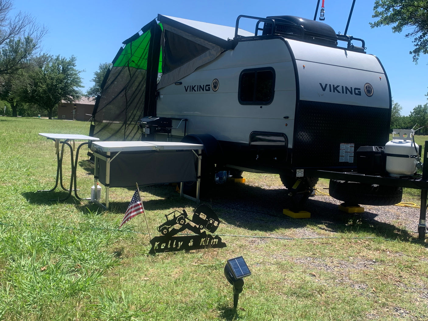 A light-colored Viking RV rental is set up for outdoor living, featuring an awning, grill, and prep table, under a clear sky.