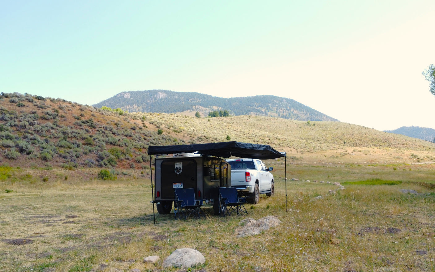RV rental: Truck and teardrop trailer with awning & chairs set up at a scenic mountain campsite.