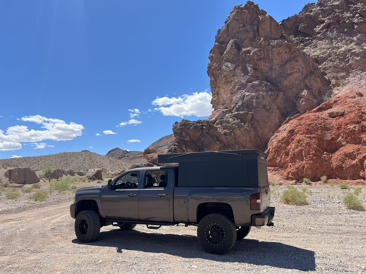 Side profile of the Oru Designs Bruin camper closed down in low-profile travel mode on the truck bed, parked below red desert rock formations — photo 2