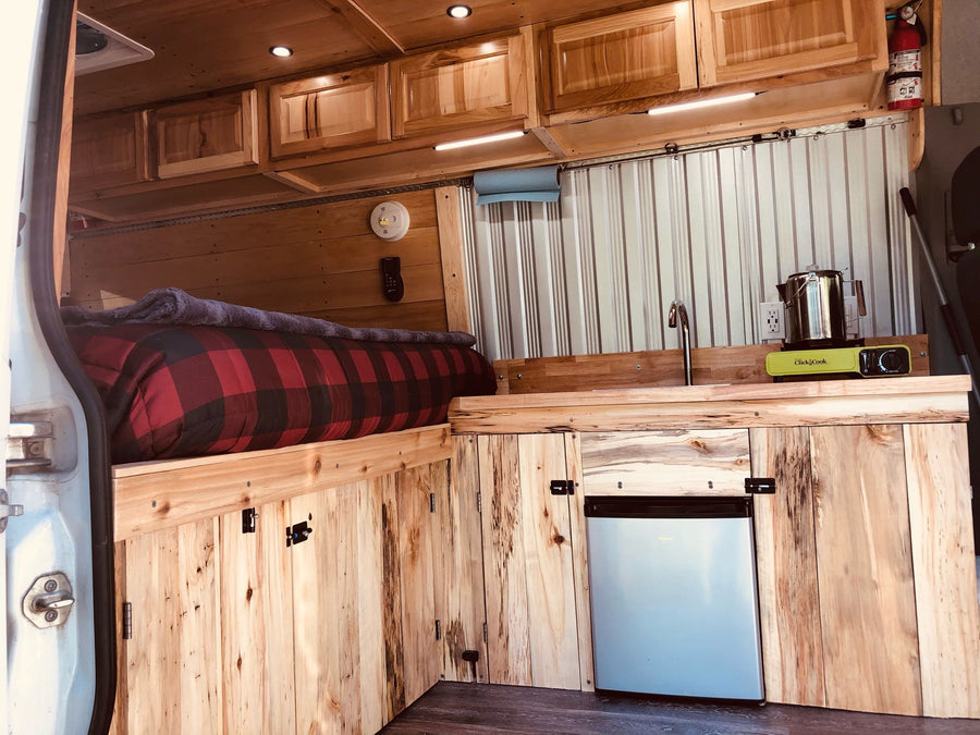 and essential safety features for comfortable travel.|RV rental: This custom wooden van interior offers a cozy plaid bed & functional kitchen with sink