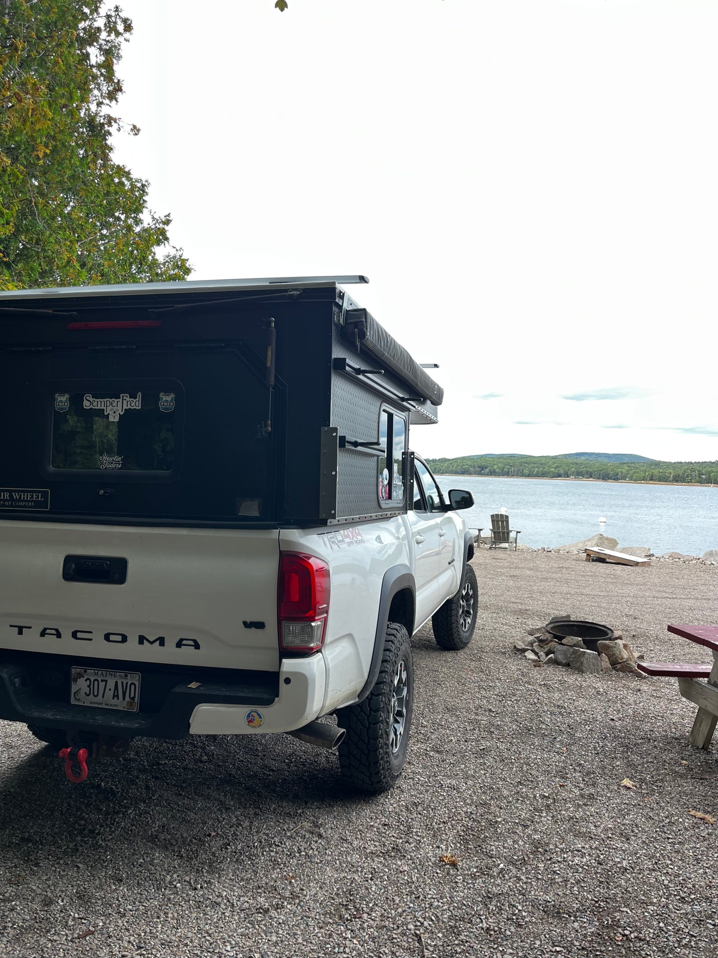 White Toyota Tacoma with a pop-top truck camper, an excellent rv rental for lakeside camping in Maine with a fire pit.