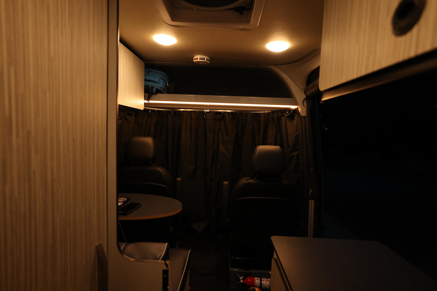 Inside this RV rental: front seats swivel to a dining table. Warm lighting, privacy curtains, and overhead storage.