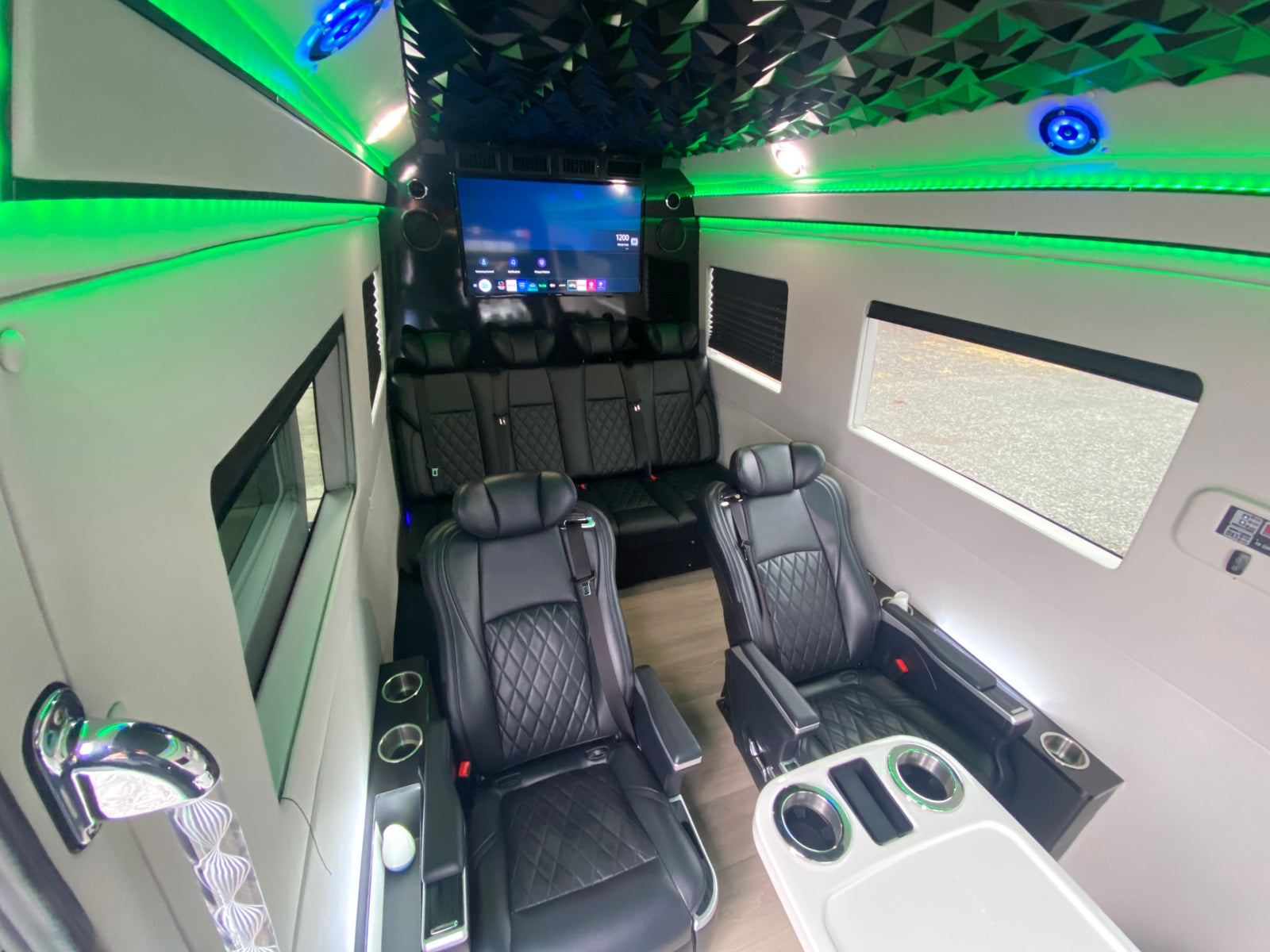 Luxury RV rental interior: black leather diamond-stitched seats, vibrant green LED lighting, large TV, and modern design.