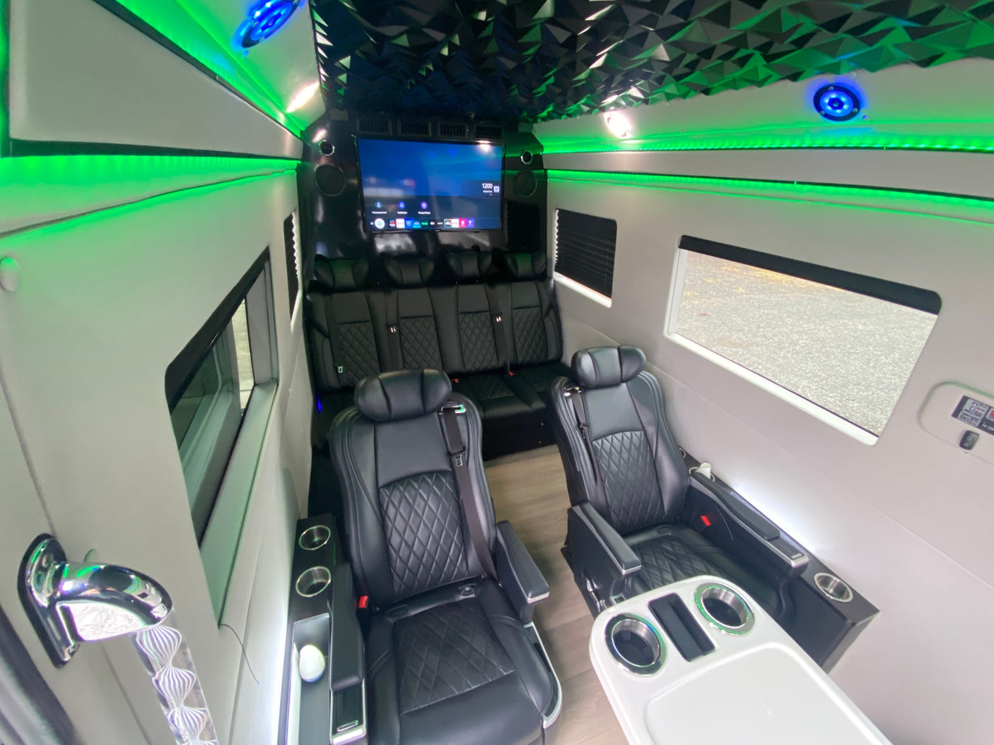 Luxury RV rental interior: black leather diamond-stitched seats, vibrant green LED lighting, large TV, and modern design.