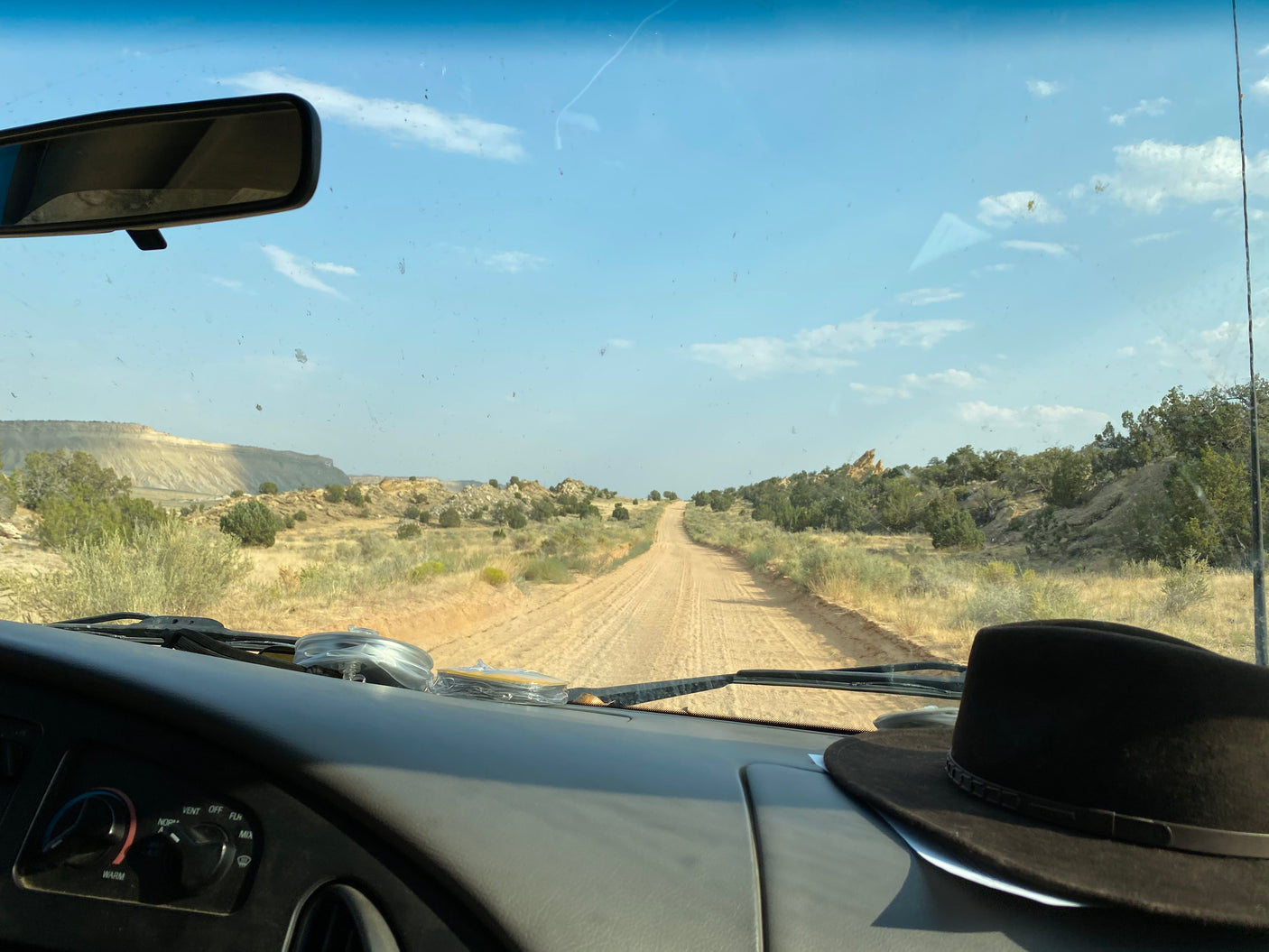 Enjoying the dusty road view from an RV rental, dashboard and hat in foreground, vast desert landscape beyond.