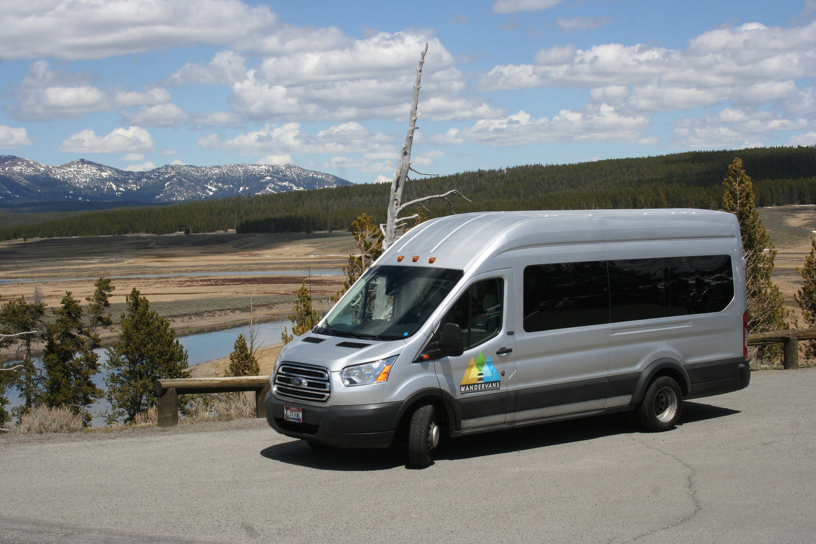 Silver Wandervans RV rental van overlooks a scenic river, forest, and snowy mountains under a partly cloudy sky.