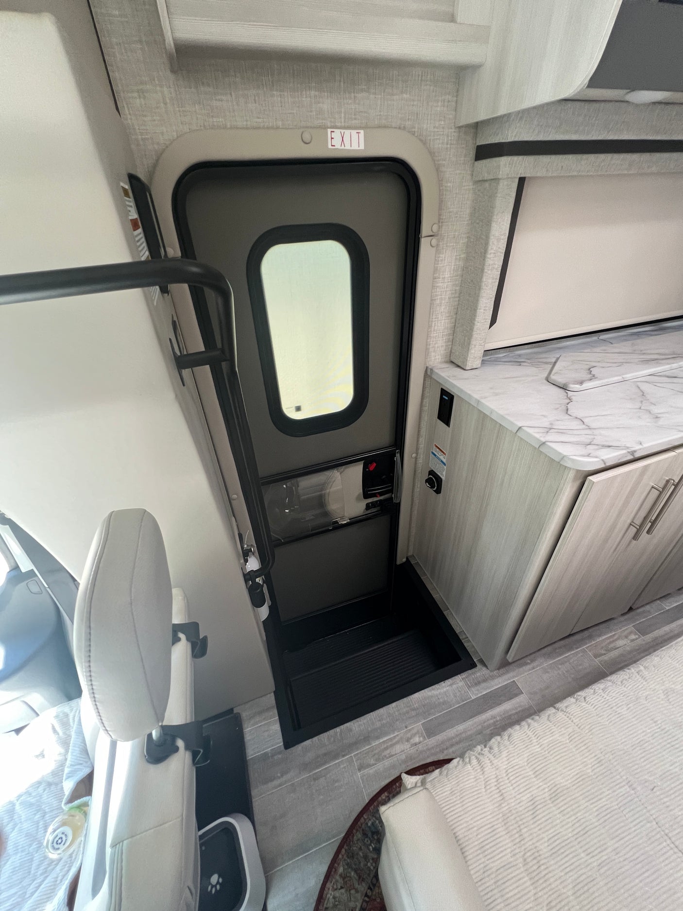 Inside an RV rental, showing the main entry door, "EXIT" sign, kitchenette, and part of the living/sleeping area.