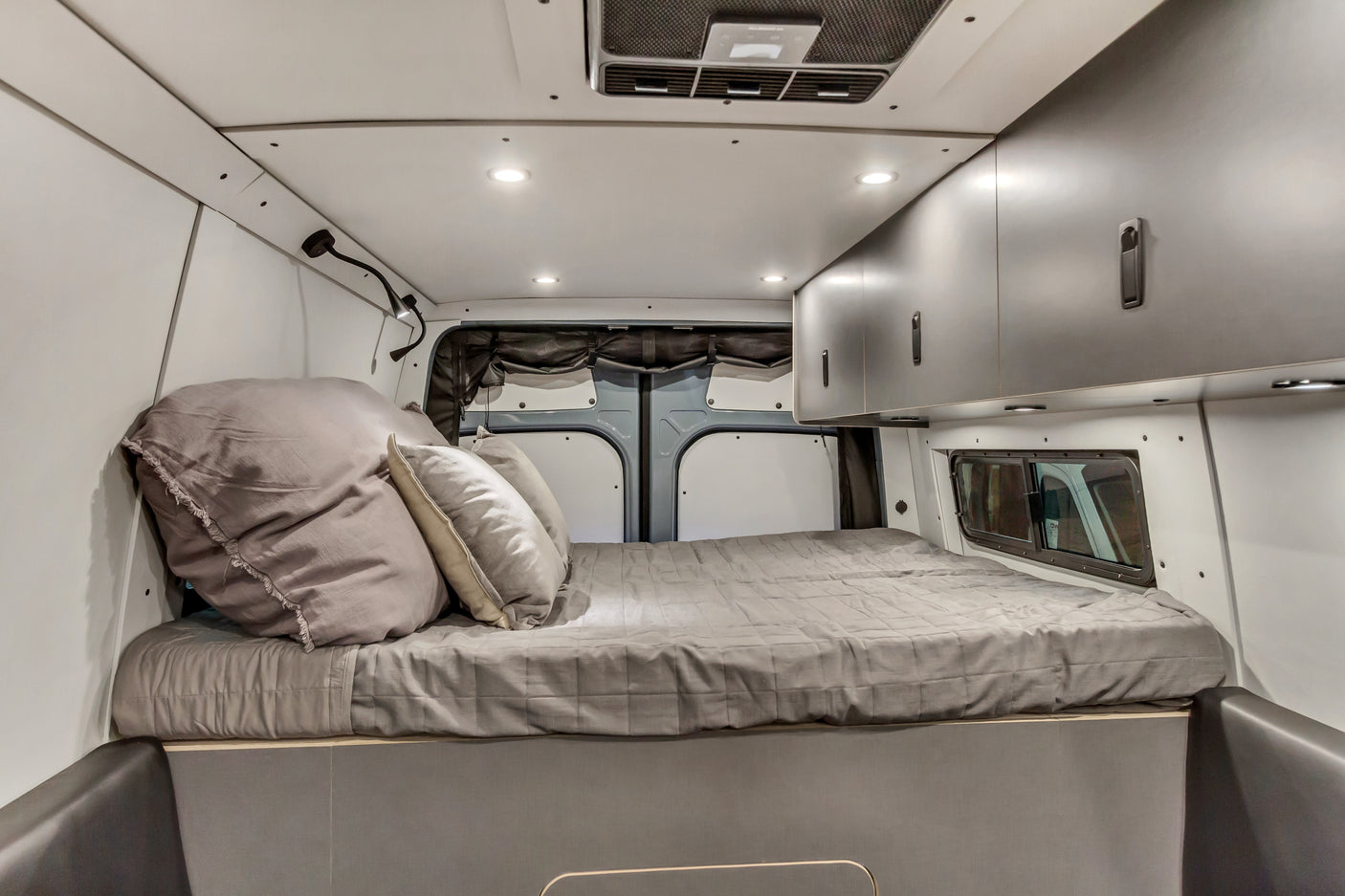 This RV rental's cozy campervan interior features a comfy bed, overhead storage, and ambient lighting.