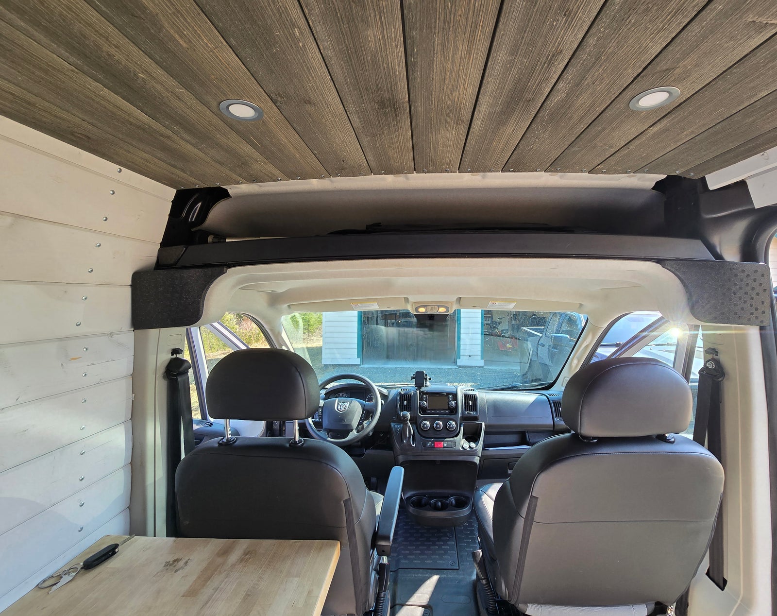 Custom RV rental camper van interior featuring wooden plank ceiling, white paneled walls, and the front driver's area.