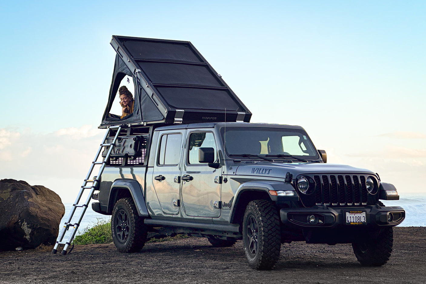 Jeep Gladiator with rooftop tent for an RV rental. A person in the tent enjoys ocean views from this ultimate overlanding setup.