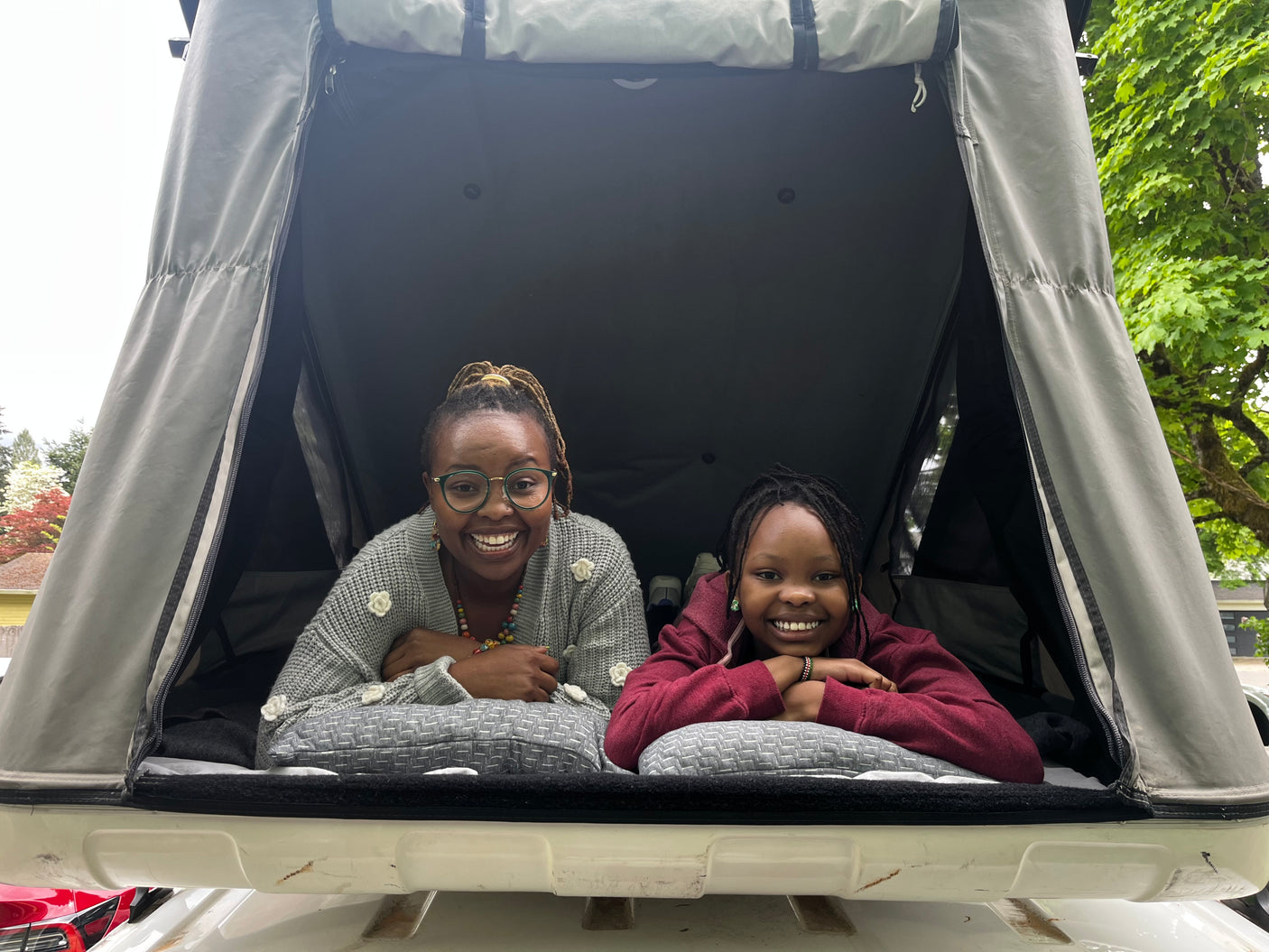 Two joyful people, an adult and child, inside an RV rental rooftop tent, smiling at the camera. Ideal for family camping trips.