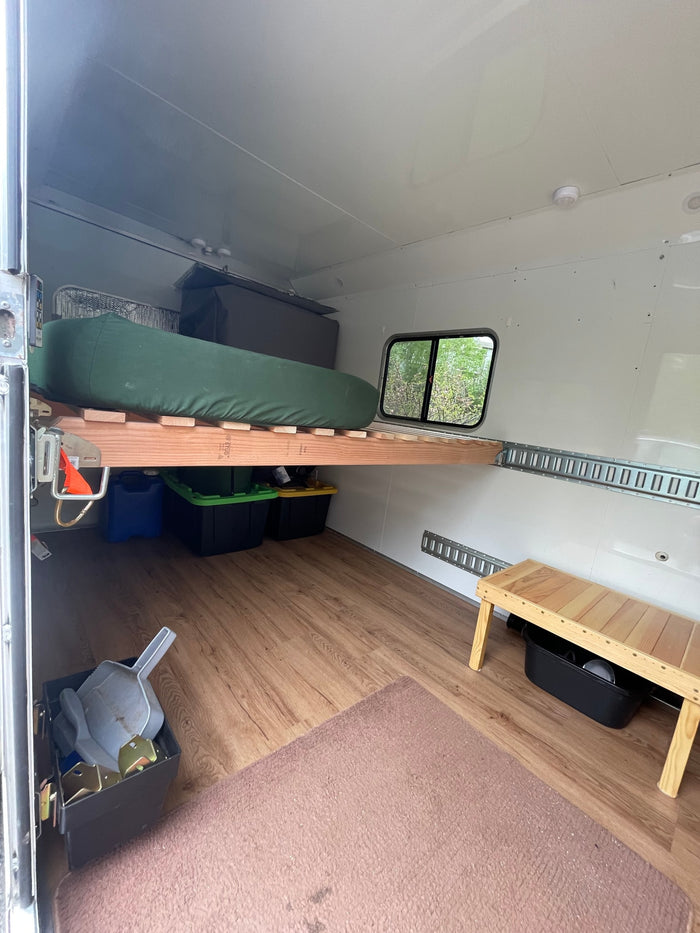 Spacious RV rental interior featuring a wooden bed platform with storage underneath, a window, and wood laminate flooring.