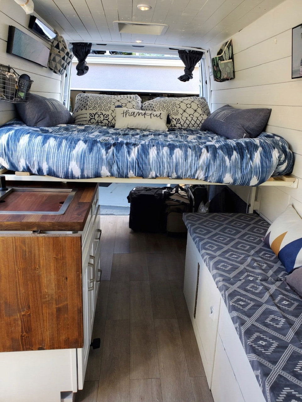 Cozy RV rental interior featuring an elevated bed with blue bedding, a compact kitchen, and side bench seating. — photo 4
