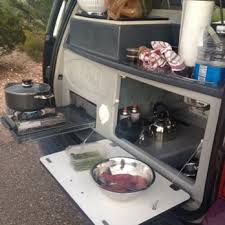 RV rental's rear reveals a compact travel kitchen: built-in sink, outdoor stove cooking with a pot & cutting board.