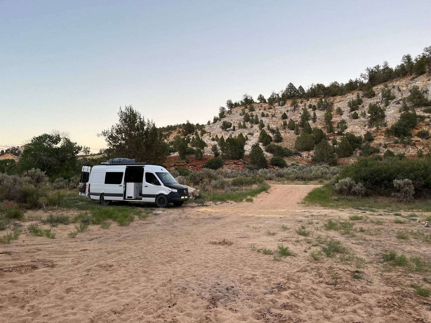 RV rental camper van parked on a sandy track in a desert landscape, ready for adventure amidst rocky hills and trees.