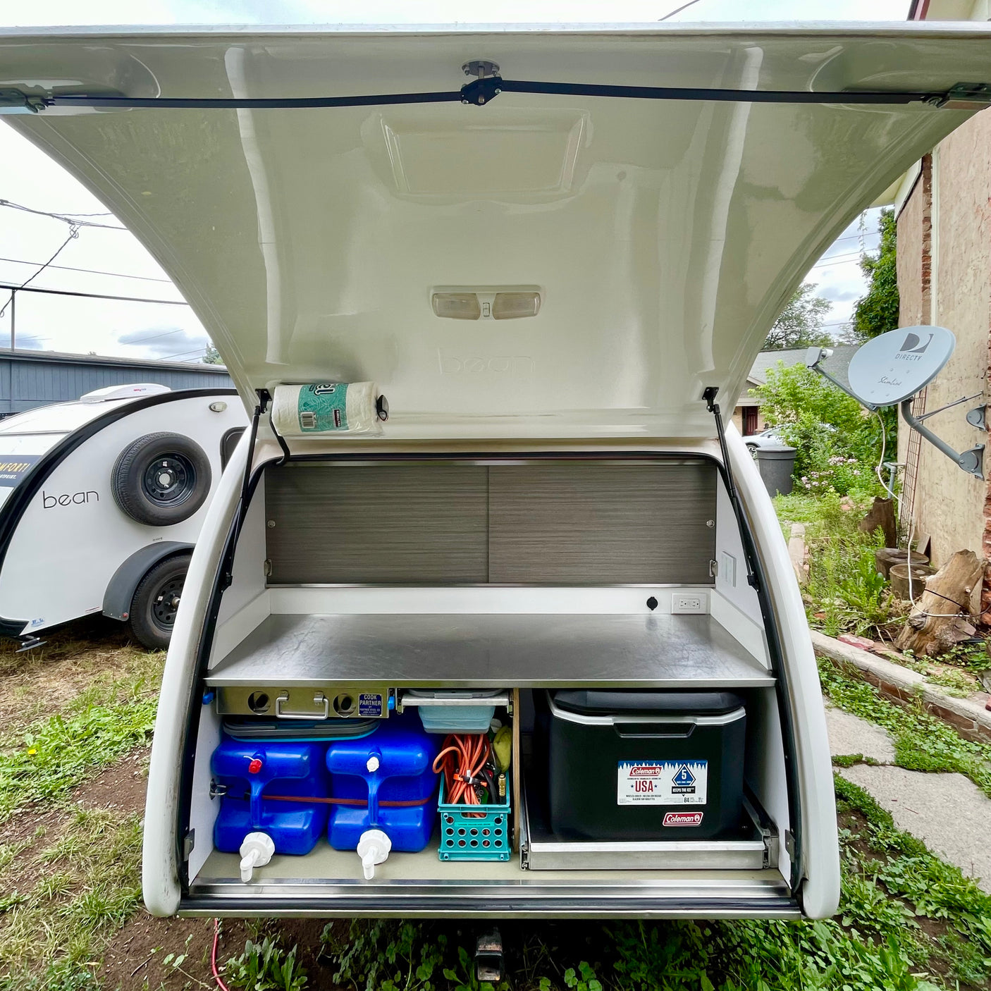 RV rental teardrop camper galley, featuring a compact kitchen with water tanks and a cooler for camping.