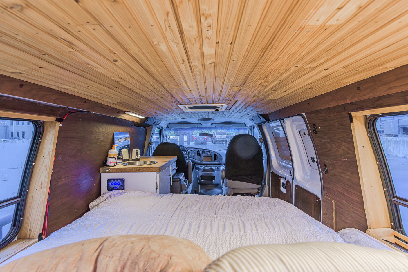 Cozy rv rental camper van interior with wood paneling, bed, small kitchen, and front cab view. Ideal for van life adventures.