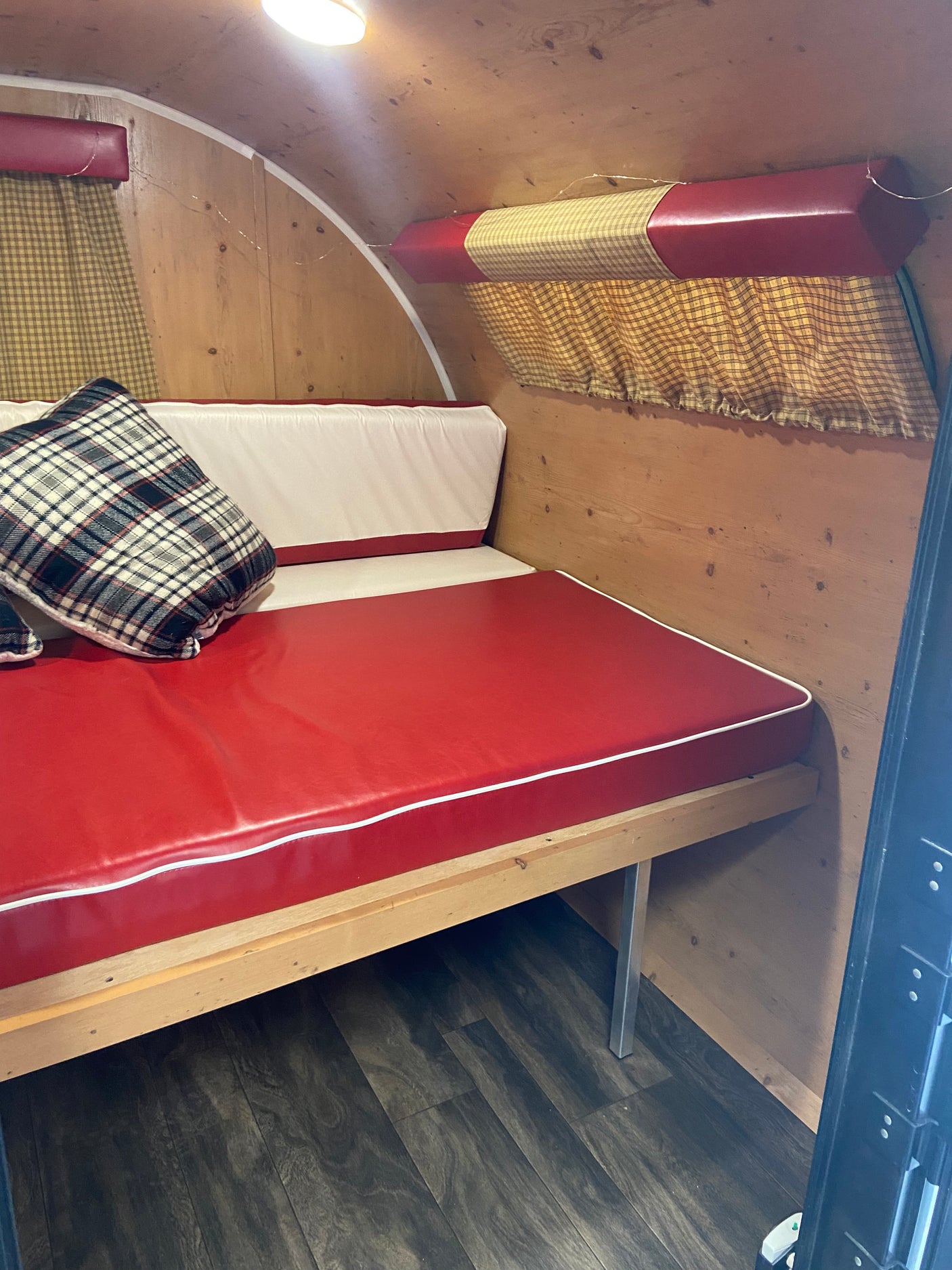 Cozy RV rental interior with a red and white upholstered bench bed, plaid pillow, wooden walls, and gingham curtains.